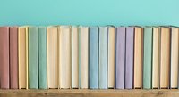Row of colorful vintage books arranged on wooden shelf against turquoise wall, creating organized library display for educational and literary content.