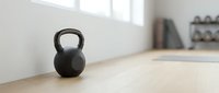 Black kettlebell weight on wooden floor in bright gym studio with natural light, suitable for fitness, training, and workout design projects.