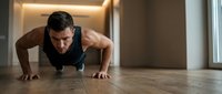 Adult male athlete performing push-up exercise on wooden floor in modern gym environment with warm lighting, demonstrating strength training and fitness routine for workout programs.