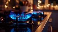 Blue gas flame burning on modern stove with bokeh lights in background, creating cozy kitchen atmosphere. Close up view shows energy consumption and cooking concept.