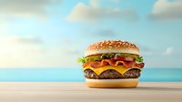 Appetizing cheeseburger with fresh vegetables and melted cheese on sesame bun against blurred tropical beach background on wooden table.