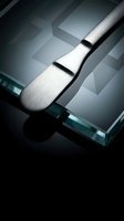 Professional makeup brush with silver handle on glass surface with dramatic lighting and geometric shadows for cosmetic and beauty applications.