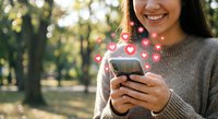Young woman using smartphone with floating heart icons in sunny park, social media engagement and digital communication concept for marketing campaigns.