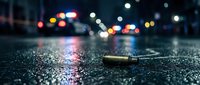 Crime scene with bullet casing on wet asphalt street at night with blurred police car lights in background for forensic investigation concepts.