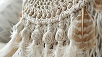 Intricate macrame wall hanging detail with delicate cotton fringe and beaded tassels in natural ivory white color showing bohemian textile craftsmanship and texture.