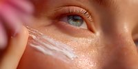 Young woman applying moisturizing cream under eye area for anti-aging skincare routine and hydration treatment.