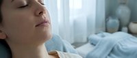 Young woman patient resting peacefully in hospital bed with eyes closed, receiving medical care in bright clinical setting for healthcare concepts.