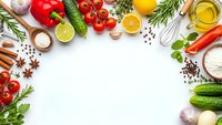 Fresh organic vegetables, herbs and cooking ingredients arranged in circular frame on white background with copy space for culinary design projects.