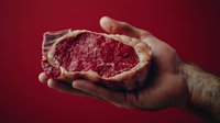 Raw ribeye steak with marbled texture held in male hand against deep red background, showcasing premium beef quality for food photography.