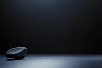 Minimalist composition with smooth stone on dark surface against black background, creating dramatic atmosphere for conceptual design projects.
