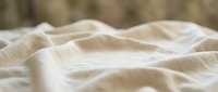 Soft beige linen fabric with natural wrinkles and folds creating gentle waves and texture for home decor and textile design projects.