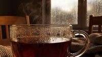 Steaming hot tea in transparent glass mug with condensation droplets on cozy indoor table setting during rainy day creating warm atmospheric mood.