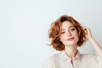Young woman with short wavy red hair and natural makeup wearing beige shirt smiling confidently against white background, looking at camera with gentle expression.