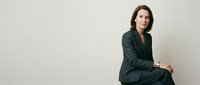 Professional businesswoman in dark green suit sitting confidently against neutral background for corporate presentations and marketing materials.