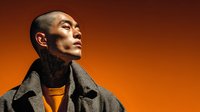 Professional Asian businessman in elegant coat looking upward with confidence against warm orange gradient background for corporate branding.