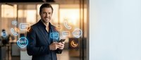 Middle-aged Caucasian male professional in dark business suit holding smartphone with floating digital communication icons including chat bubbles, phone symbols, and social media elements in modern office setting.