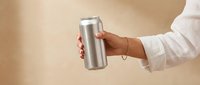 Woman holding sleek silver aluminum can against neutral beige background. Modern minimalist product presentation for beverage branding and marketing campaigns.