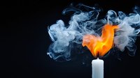 White burning candle with bright orange flame and ethereal blue smoke swirling against dark background, creating dramatic contrast and mystical atmosphere.