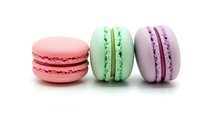 Three colorful French macarons in pink, mint green and lavender purple arranged on white background, isolated dessert cookies for bakery design.