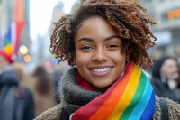Young African American woman with natural curly hair wearing rainbow scarf and gray winter coat smiling at pride parade celebration, expressing joy and authenticity.