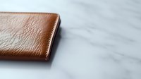 Brown leather wallet on white marble background with copy space, minimalist composition showing luxury accessory detail and texture for business and finance concepts.