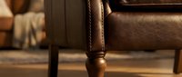 Close-up of elegant brown leather armchair leg with decorative wooden turning and stitched upholstery detail in warm interior setting for home decor.
