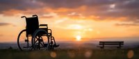 Silhouette of empty wheelchair in outdoor field at golden sunset with bench in background, symbolizing hope, recovery, accessibility, and inclusive healthcare concepts.