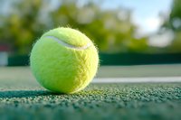 Close-up view of bright yellow tennis ball on green court surface with soft bokeh background, highlighting texture and details in natural sunlight.