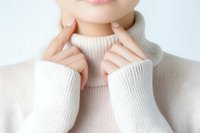 Young Asian woman wearing cozy white turtleneck sweater touching face gently, showing soft skincare and winter fashion concept. Close up studio portrait.
