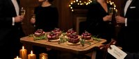 Elegant gourmet appetizers on wooden board served by professional waiters in upscale restaurant setting with warm candlelight ambiance for fine dining events.