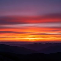 Dramatic sunset over mountain silhouettes with vibrant purple, pink and orange sky layers creating stunning natural landscape scenery for backgrounds.