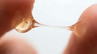 Macro shot of liquid droplet suspended between two fingers against bright backlit background, showcasing surface tension and fluid dynamics for scientific and educational content.