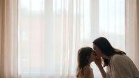 Mother and daughter sharing tender moment by window with soft natural light creating warm intimate family bonding scene for parenting and love concepts.
