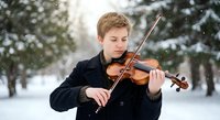 Young Caucasian male musician playing violin outdoors in snowy winter forest setting with falling snowflakes creating magical atmosphere for music education.