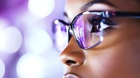 Close up portrait of young African American woman wearing glasses with purple bokeh light reflections, side view showing eye and eyewear detail.