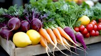 Fresh organic vegetables including purple beetroot, orange carrots, yellow onions and leafy greens arranged in wooden crate for healthy cooking and nutrition.
