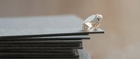Clear crystal diamond sitting on stack of dark papers with soft blurred background for luxury jewelry business concepts and precious stone marketing materials.