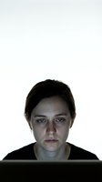 Young woman with bruised face looking at laptop screen in dark room showing domestic violence aftermath for awareness campaigns.