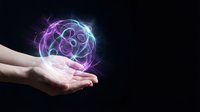 Glowing neon energy sphere with swirling purple and blue light effects floating above open human hands against dark background for futuristic technology concepts.