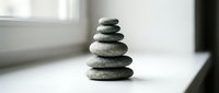 Balanced stack of smooth river stones creating zen meditation tower on white surface near window with natural light for mindfulness and wellness concepts.
