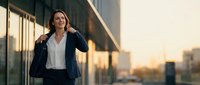 Professional businesswoman in navy suit walking confidently through modern office building corridor during golden hour sunset for corporate success concepts.