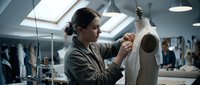 Young female fashion designer working on dress form in modern atelier studio. Professional seamstress adjusting garment on mannequin in bright workspace.