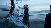 Middle-aged woman with gray hair, Caucasian ethnicity, wearing dark business attire, boarding a private jet on tarmac with mountains visible in background. Luxury travel and executive lifestyle concept.