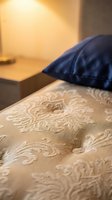 Beige damask patterned bedding with navy blue pillow on bed in warm-lit bedroom interior, suitable for hospitality and home decor design.
