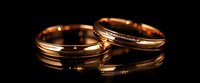 Elegant gold wedding bands with diamond accents on black reflective surface, symbolizing eternal love and commitment in matrimonial ceremony.