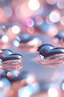 Macro water drops with soft pink and blue bokeh background creating romantic atmosphere. Reflective surface shows delicate light patterns and abstract shapes.