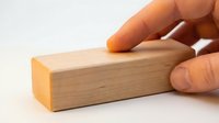 Caucasian male hand pressing down on a smooth rectangular wooden block on a white surface, concept of control, stability, and precision.