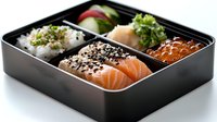 Fresh salmon nigiri and rice bento box with red caviar, black sesame seeds, and green herbs garnish served in traditional Japanese compartment container.