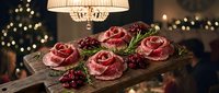 Raw beef steaks arranged on wooden board with rosemary herbs and cranberries in elegant dining room with warm bokeh lights for holiday cooking.