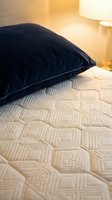 Dark navy velvet pillow resting on beige quilted mattress with warm ambient lighting from bedside lamp, creating cozy bedroom atmosphere for home decor and interior design.